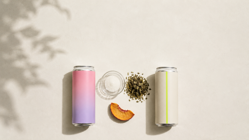 Two aluminum cans side by side, pastel pink-lavender left and cream with lime accent right, with dishes of caffeine crystals and green tea leaves between them.